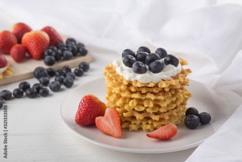 Delicious waffles with fresh fruit and berries on a white wooden table. Waffles with strawberries and blueberries. Free space for text. Traditional belgian waffles with fresh fruit. Stack of waffles w Delicious waffles with fresh fruit and berries on a white wooden table. Waffles with strawberries and blueberries. Free space for text. Traditional belgian waffles with fresh fruit. Stack of waffles w