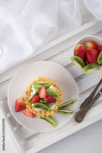 Delicious waffles with fresh fruit and berries on a white wooden table. Waffles with strawberries, kiwi, banana, cream. Free space for text. Traditional belgian waffles with fresh fruit. Stack of waff