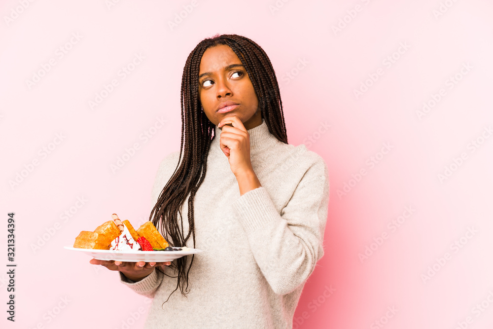 Young african american woman holding a waffle isolated looking sideways with doubtful and skeptical expression. Young african american woman holding a waffle isolated looking sideways with doubtful and skeptical expression.