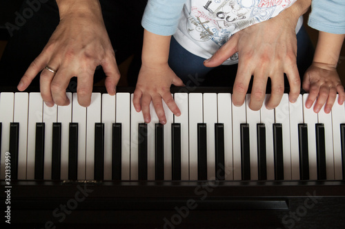 father and son playing the piano. small and big hands on a keyboard. top shot