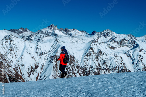 Tourist with backpack and trekking poles walking walking in the snowy mountains at sunny day