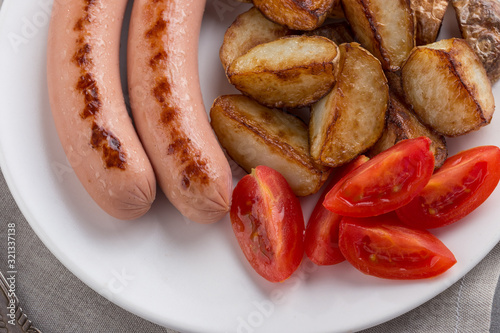 Close-up shot of fried potatoes with sausages and egg. Breakfast. Potatoes with sausages fried in oil, in rustic style. Frying pan with tasty cooked egg and sausages on table