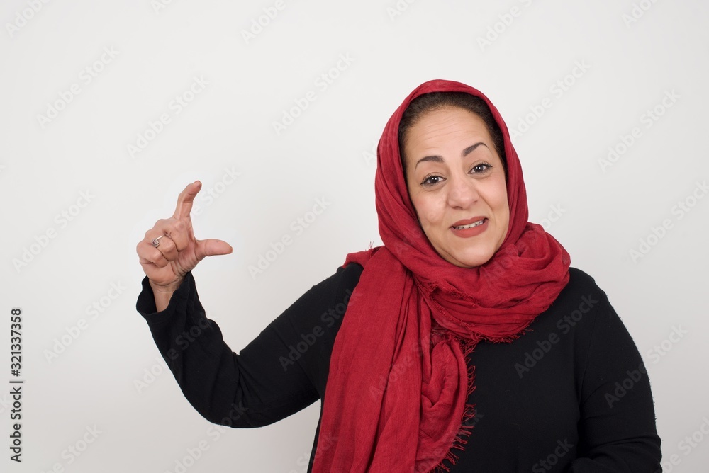 Muslim woman over isolated background gesturing with hand showing small size, measure symbol. Smiling looking at the camera. Measuring concept. Muslim woman over isolated background gesturing with hand showing small size, measure symbol. Smiling looking at the camera. Measuring concept.