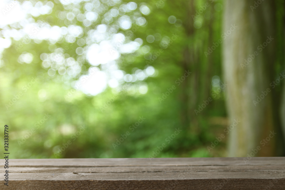 Image of grey wooden table in front of abstract blurred background of green leaves and trees Image of grey wooden table in front of abstract blurred background of green leaves and trees