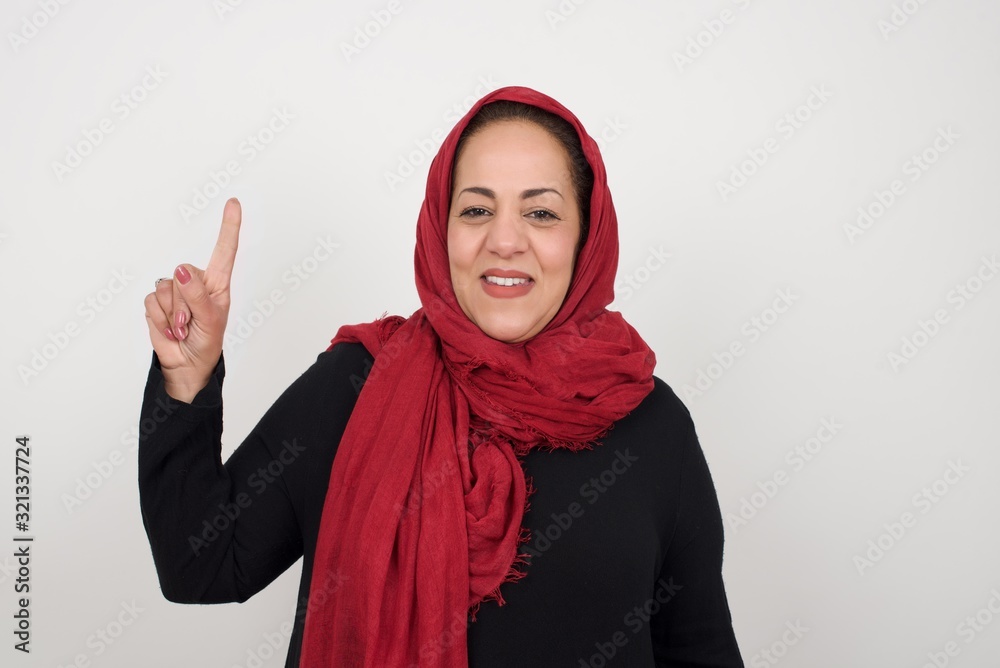Young muslim woman standing against gray wall showing and pointing up with fingers number one while smiling confident and happy. Young muslim woman standing against gray wall showing and pointing up with fingers number one while smiling confident and happy.