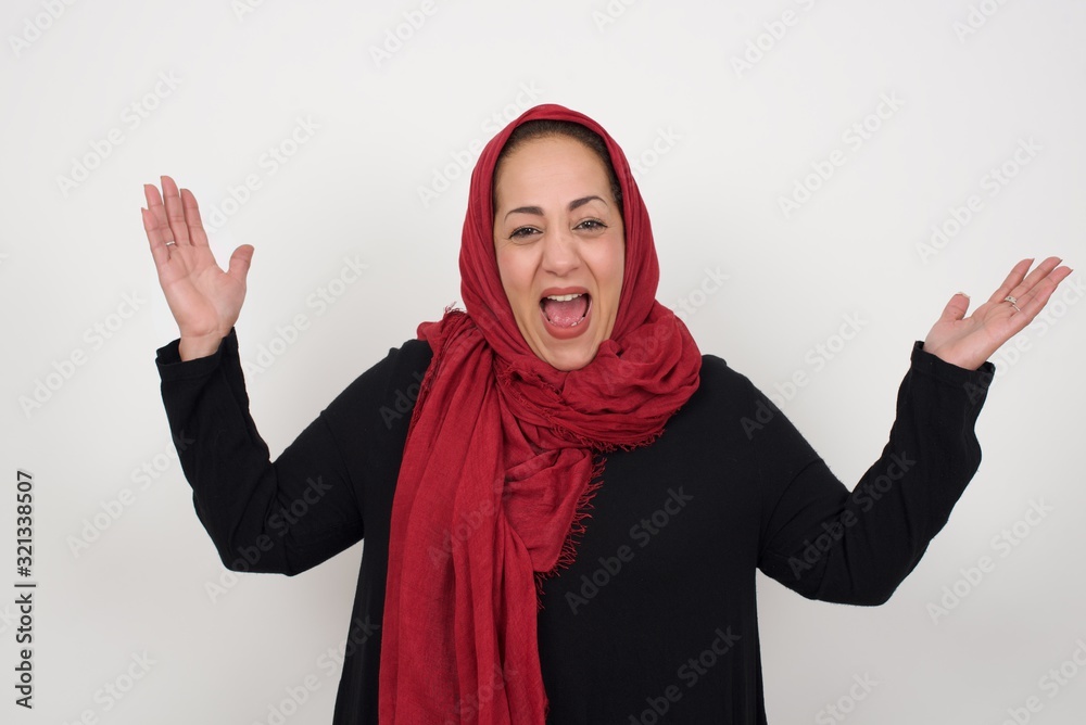 Portrait of beautiful female looks with excitement at camera, keeps hands raised over head, notices something unexpected, isolated over gray wall. Lovely woman reacts on sudden news.