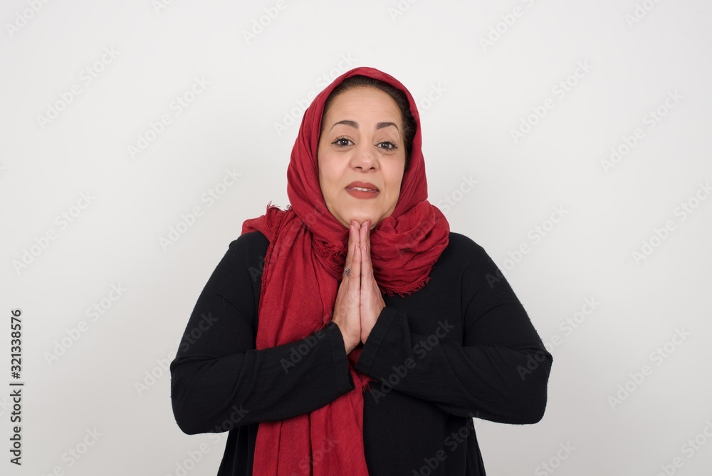 Horizontal portrait of pretty muslim woman keeps palms together, has pleased expression. Glad attractive female makes request, pleads for mercy. Hopeful young adult. Horizontal portrait of pretty muslim woman keeps palms together, has pleased expression. Glad attractive female makes request, pleads for mercy. Hopeful young adult.