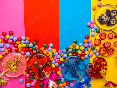 lollipops with flowers and berries on colorful background. Elder, violet, cornflower, raspberries, cranberries, wild strawberries. Multicolored mixed chocolate candies