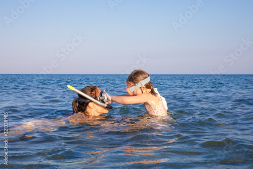 little girl playing with woman, both with diving glasses to snorkeling, in the water of Genoveses Beach, in Cabo de Gata Natural Park (Almeria, Andalusia, Spain)