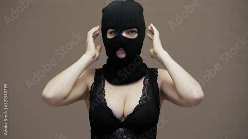 Sexy funny woman puts on hacker black balaclava mask, dressed in lace bra, robbery concept