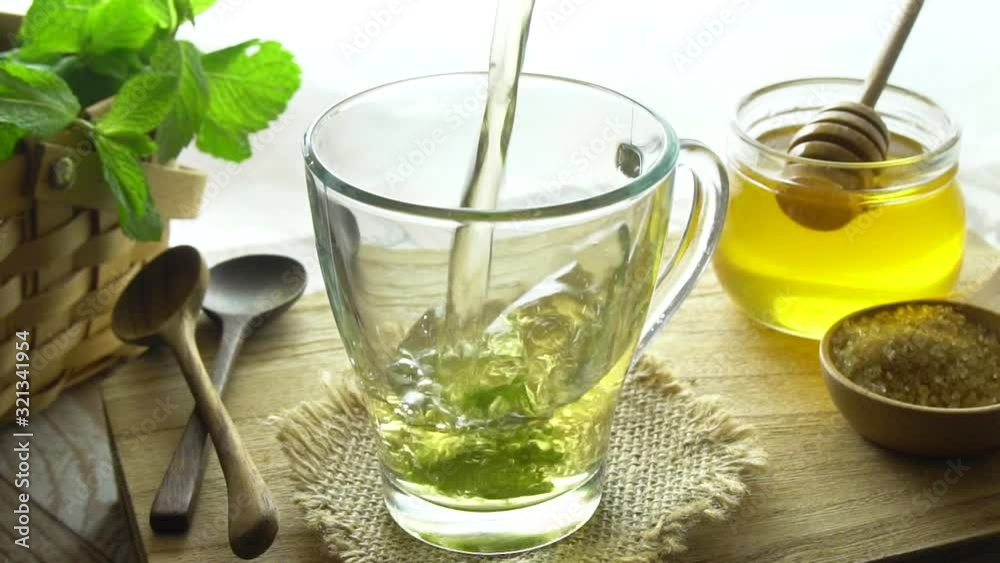 Mint tea being poured into cup. Slow motion shot. Honey in the background. Mint tea is a healthy source of vitamins such as manganese and a natural medicine. Mint tea being poured into cup. Slow motion shot. Honey in the background. Mint tea is a healthy source of vitamins such as manganese and a natural medicine.