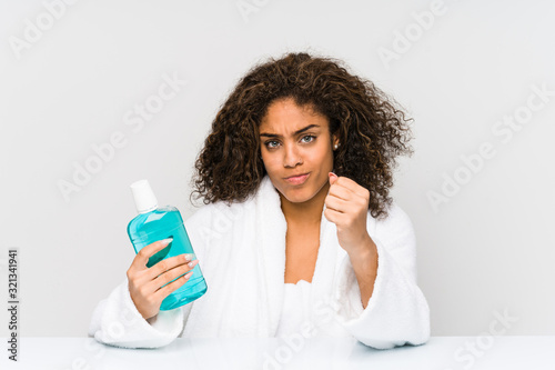 Young african american woman holding a mouth wash showing fist to camera, aggressive facial expression.