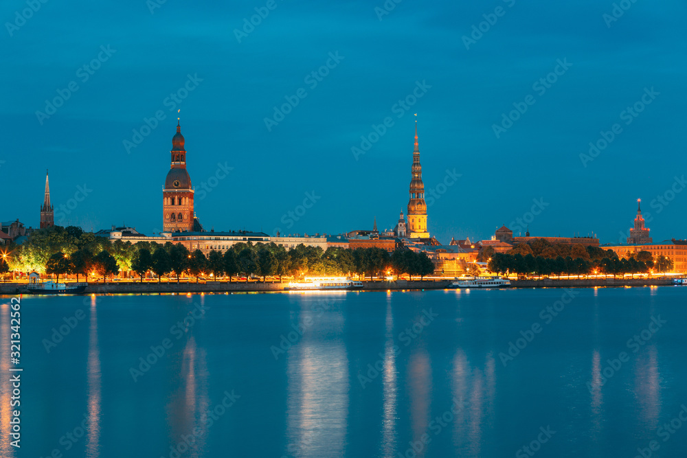 Riga, Latvia. Panoramic Picturesque Urban View Of Daugava Or Western Dvina River In Central Part Of City With Famous Landmarks In Bright Illumination Under Blue Sky In Summer Night
