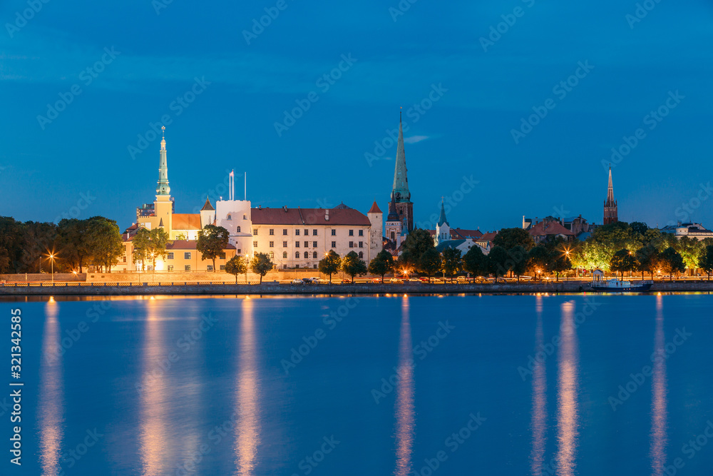 Riga, Latvia. Panoramic Picturesque Urban View Of Daugava Or Western Dvina River In Central Part Of City With Famous Landmarks In Bright Illumination Under Blue Sky In Summer Night