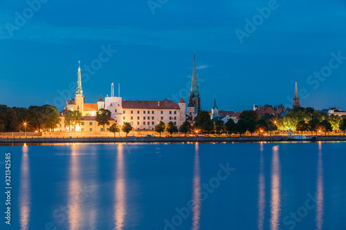 Riga, Latvia. Panoramic Picturesque Urban View Of Daugava Or Western Dvina River In Central Part Of City With Famous Landmarks In Bright Illumination Under Blue Sky In Summer Night