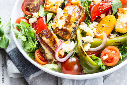 Vegetable salad cherry tomatoes, baked pepper, salad mix and onion with grilled haloumi (halloumi) cheese. Keto diet, healthy food. Light grey stone background. Close up.