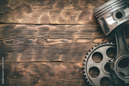 Old car engine piston with connecting rod and cog wheel on wooden workbench background with copy space. Machinery abstract background. photo