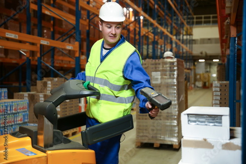 warehouse worker on a forklift scans a box of goods with a barcode scanner