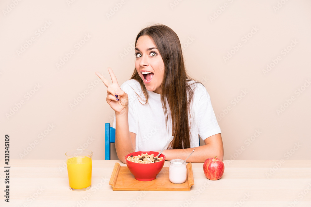 Young caucasian woman having a breakfast isolated joyful and carefree showing a peace symbol with fingers. Young caucasian woman having a breakfast isolated joyful and carefree showing a peace symbol with fingers.