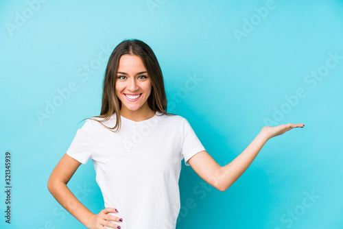 Young caucasian woman  isolated showing a copy space on a palm and holding another hand on waist.