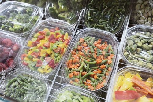 Frozen vegetables, fruits and berries. Food products are poured into rectangular plastic trays. photo
