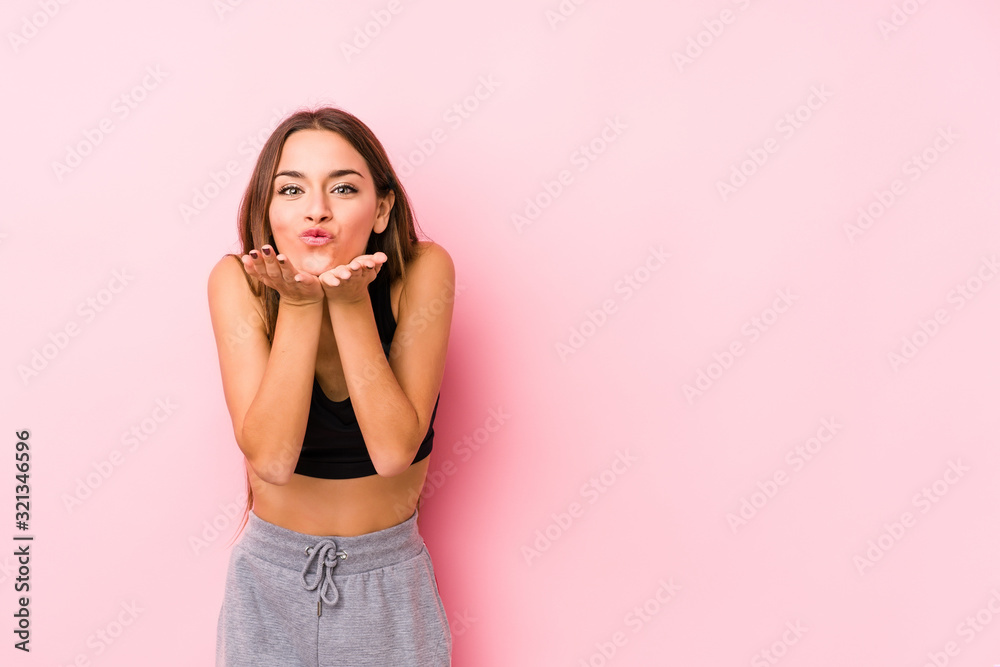 Young caucasian fitness woman posing in a pink background folding lips and holding palms to send air kiss. Young caucasian fitness woman posing in a pink background folding lips and holding palms to send air kiss.