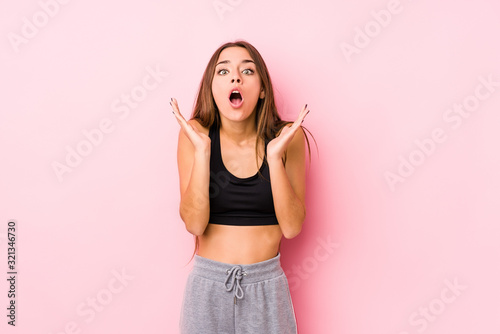 Young caucasian fitness woman posing in a pink background surprised and shocked. © Asier