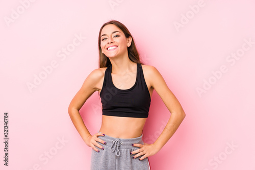 Young caucasian fitness woman posing in a pink background confident keeping hands on hips.