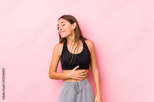 Young caucasian fitness woman posing in a pink background touches tummy, smiles gently, eating and satisfaction concept.