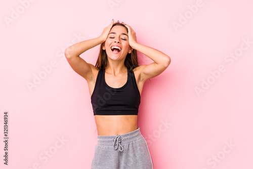 Young caucasian fitness woman posing in a pink background laughs joyfully keeping hands on head. Happiness concept.