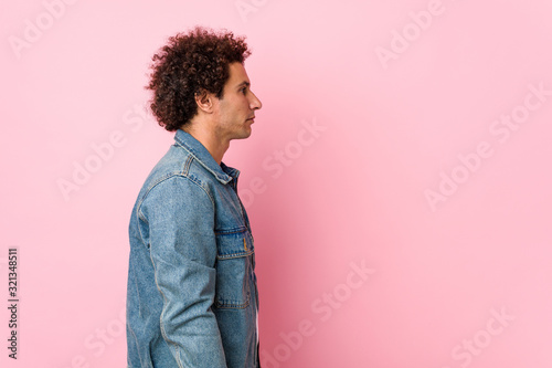 Curly mature man wearing a denim jacket against pink background gazing left, sideways pose. photo