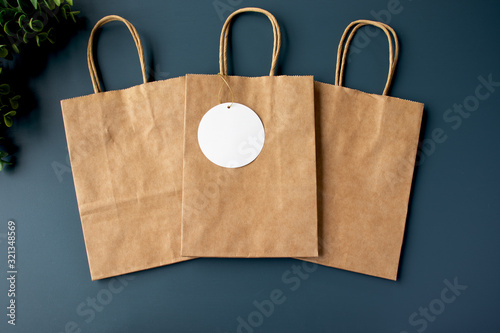 Three paper kraft bags with a blank gift tag on a blue background mockup photo