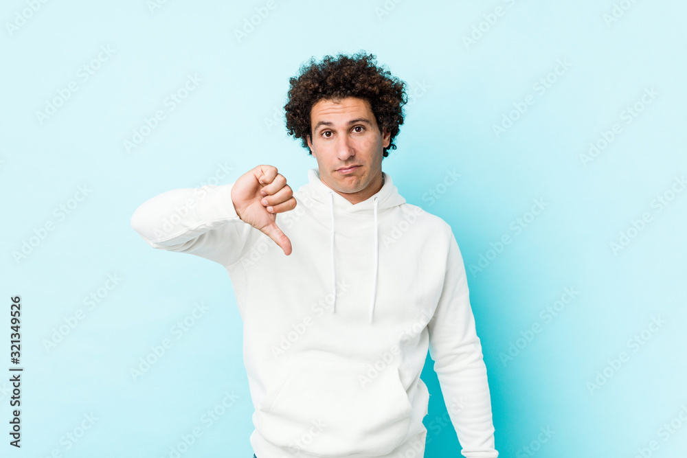 Young sporty man against a blue background showing a dislike gesture, thumbs down. Disagreement concept. Young sporty man against a blue background showing a dislike gesture, thumbs down. Disagreement concept.