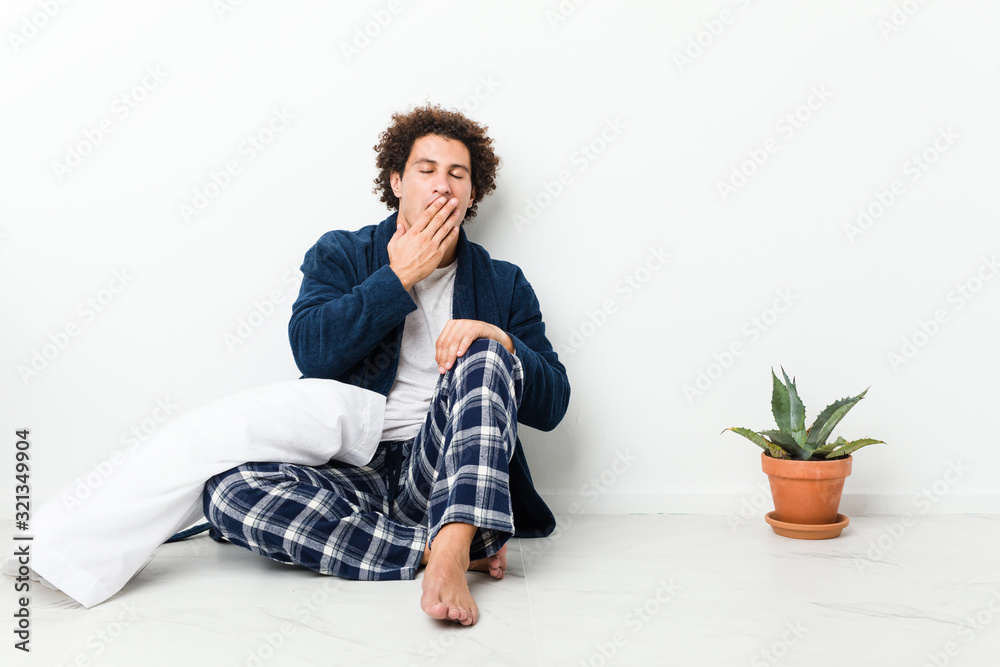 Mature man wearing pajama sitting on house floor yawning showing a tired gesture covering mouth with hand. Mature man wearing pajama sitting on house floor yawning showing a tired gesture covering mouth with hand.