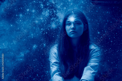 Dark-haired girl against the starry sky with a thoughtful look. A star is burning in the girl's forehead as a symbol of clairvoyance. Tinting in classic blue. starry background is from the NASA site
