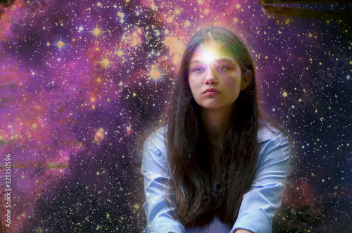 Dark-haired girl against the starry sky with a thoughtful look. A star is burning in the girl's forehead as a symbol of clairvoyance. Selective focus. Art processing. The starry background is taken fr photo