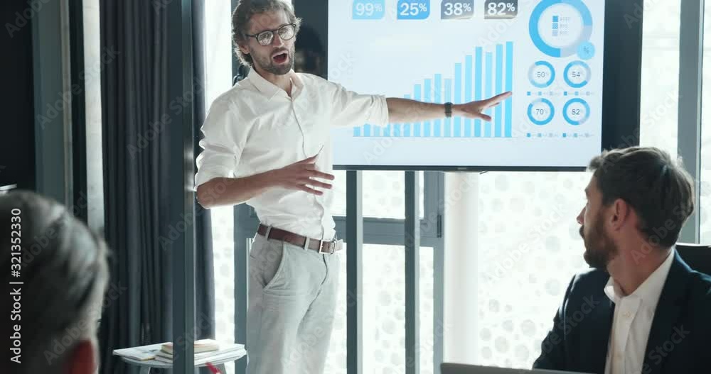 Young Bearded IT worker standing by the Glass Board with different Notes, Touching multicolor papers. Looking Serious and Confident. Close up view of Handsome Businessman, standing indoor Office.