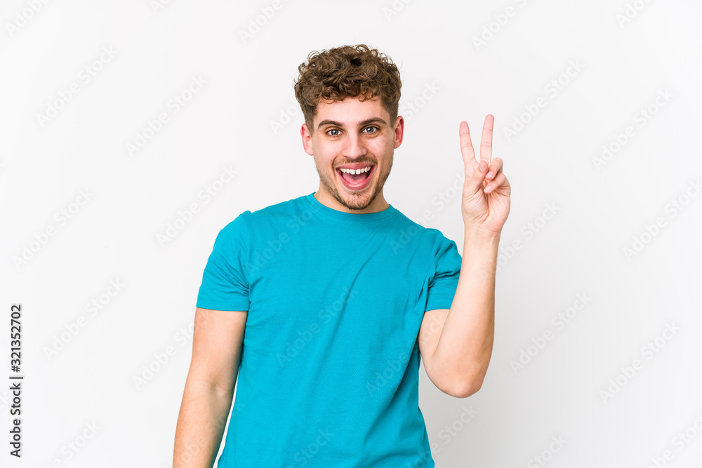 Young blond curly hair caucasian man isolated joyful and carefree showing a peace symbol with fingers. Young blond curly hair caucasian man isolated joyful and carefree showing a peace symbol with fingers.