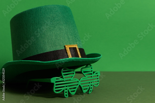 Happy St Patricks Day. Lepricon hat with glasses in the shape of a three leaf clover on a green background. Holiday attributes