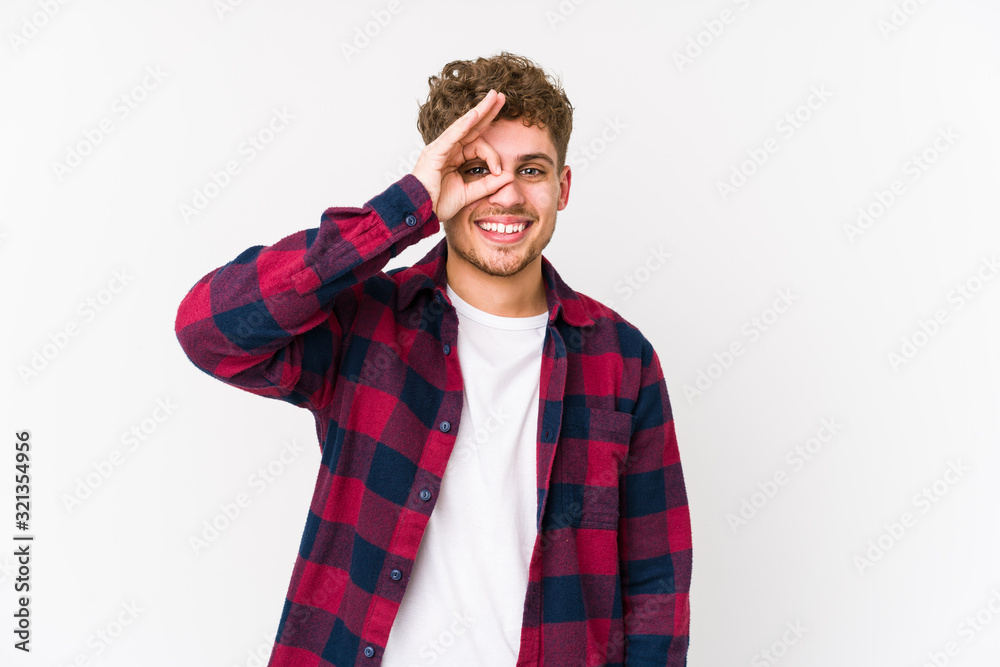 Young blond curly hair caucasian man isolated excited keeping ok gesture on eye. Young blond curly hair caucasian man isolated excited keeping ok gesture on eye.