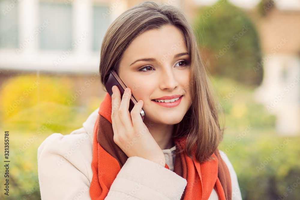 Cellphone talk. Beautiful woman talking on the phone outdoors and smiling toothy smile. mixes race asian russian model on green city scape background at the station in city of Brussels Belgium