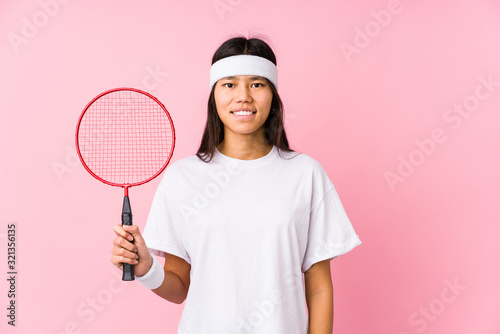 Young chinese woman playing badminton in a pink background happy, smiling and cheerful. © Asier