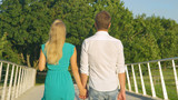 CLOSE UP Unrecognizable man and woman in love hold hands while crossing a bridge