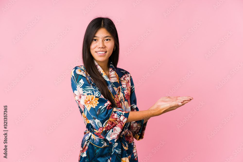 Young asian woman wearing a kimono pajamas holding a copy space on a palm. Young asian woman wearing a kimono pajamas holding a copy space on a palm.