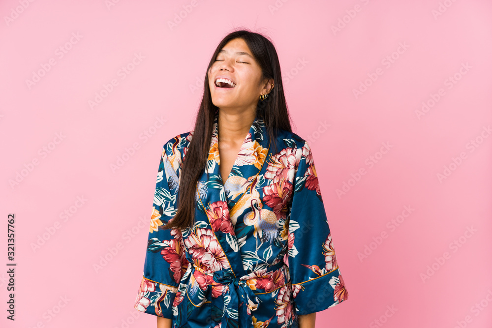Young asian woman wearing a kimono pajamas relaxed and happy laughing, neck stretched showing teeth. Young asian woman wearing a kimono pajamas relaxed and happy laughing, neck stretched showing teeth.