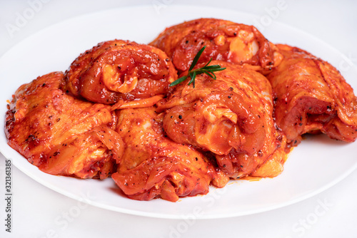 Chicken legs in a red marinade on a white plate. Top view. Chicken meat close-up.Dietary meat. Cooking.Raw marinated chicken legs for grill and bbq.Isolate. photo