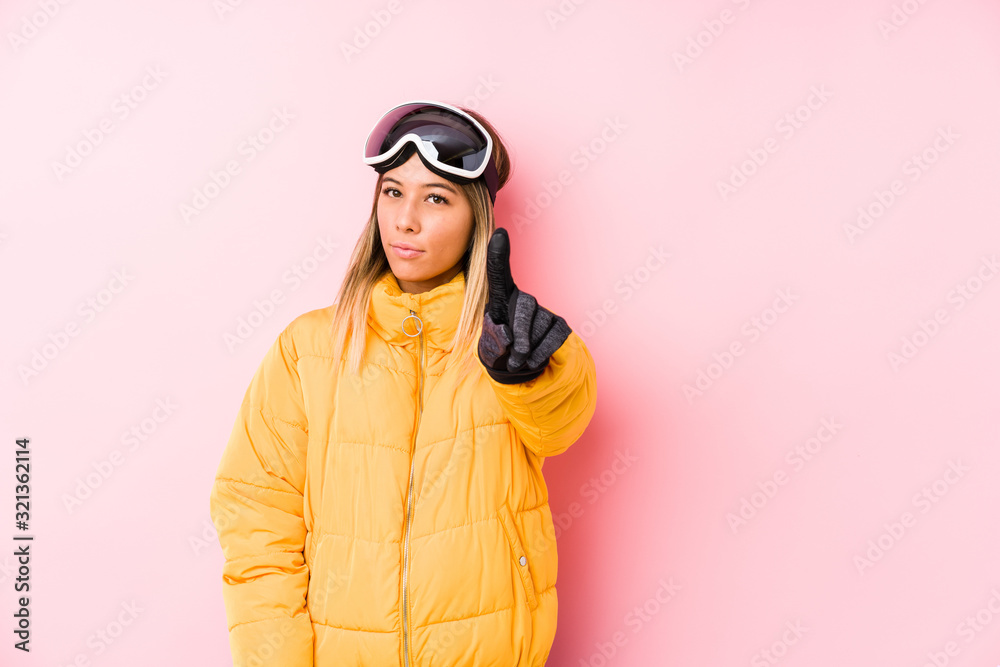 Young caucasian woman wearing a ski clothes in a pink background showing number one with finger.