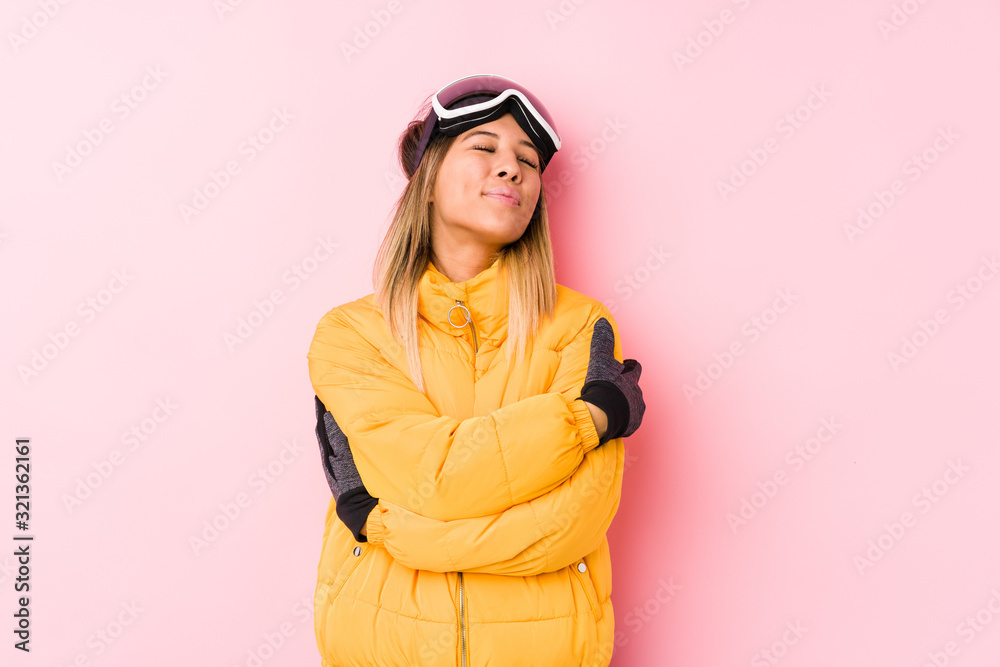 Young caucasian woman wearing a ski clothes in a pink background hugs, smiling carefree and happy. Young caucasian woman wearing a ski clothes in a pink background hugs, smiling carefree and happy.