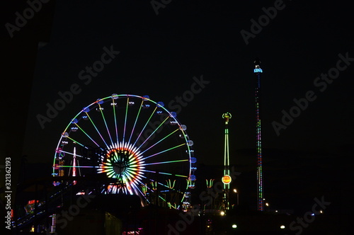 Feria de noche, al fondo la rueda de la fortuna iluminada y juegos