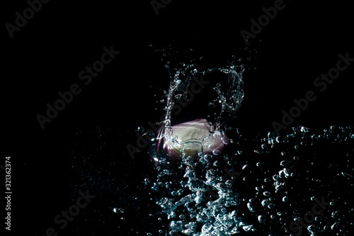The onion cut in half, purple, fresh and white fell into the water until the water spread, creating beautiful bubbles in a black background.